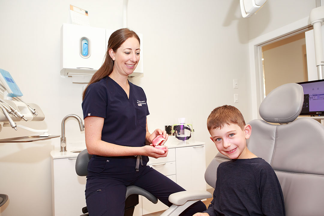 a woman holding a model of a boy in a dental chair